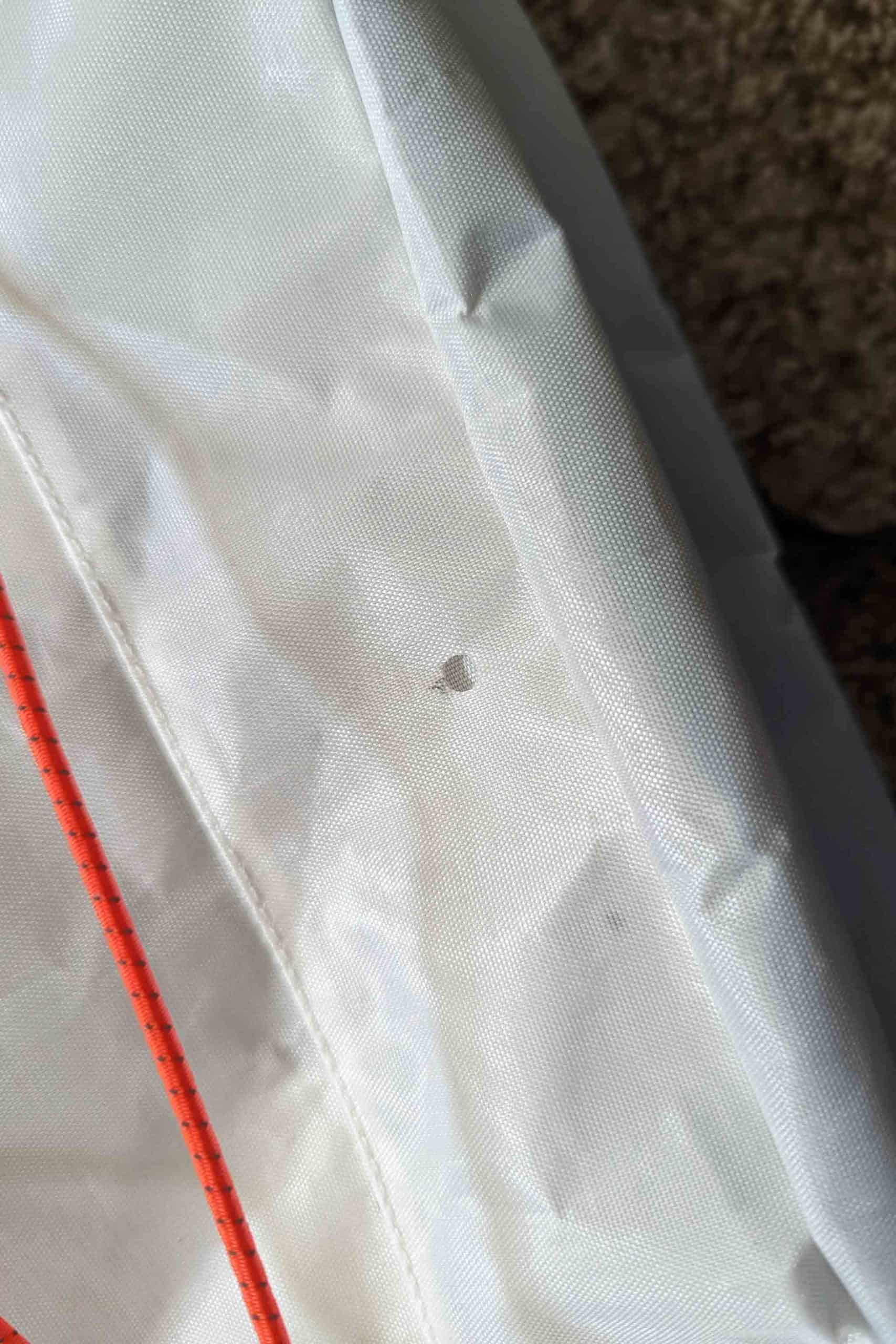 A close-up of white fabric with a small hole in the center, featuring red stitching running vertically along the left—part of a Rogue Panda Blue Ridge Handlebar Harness against a darker, textured background.