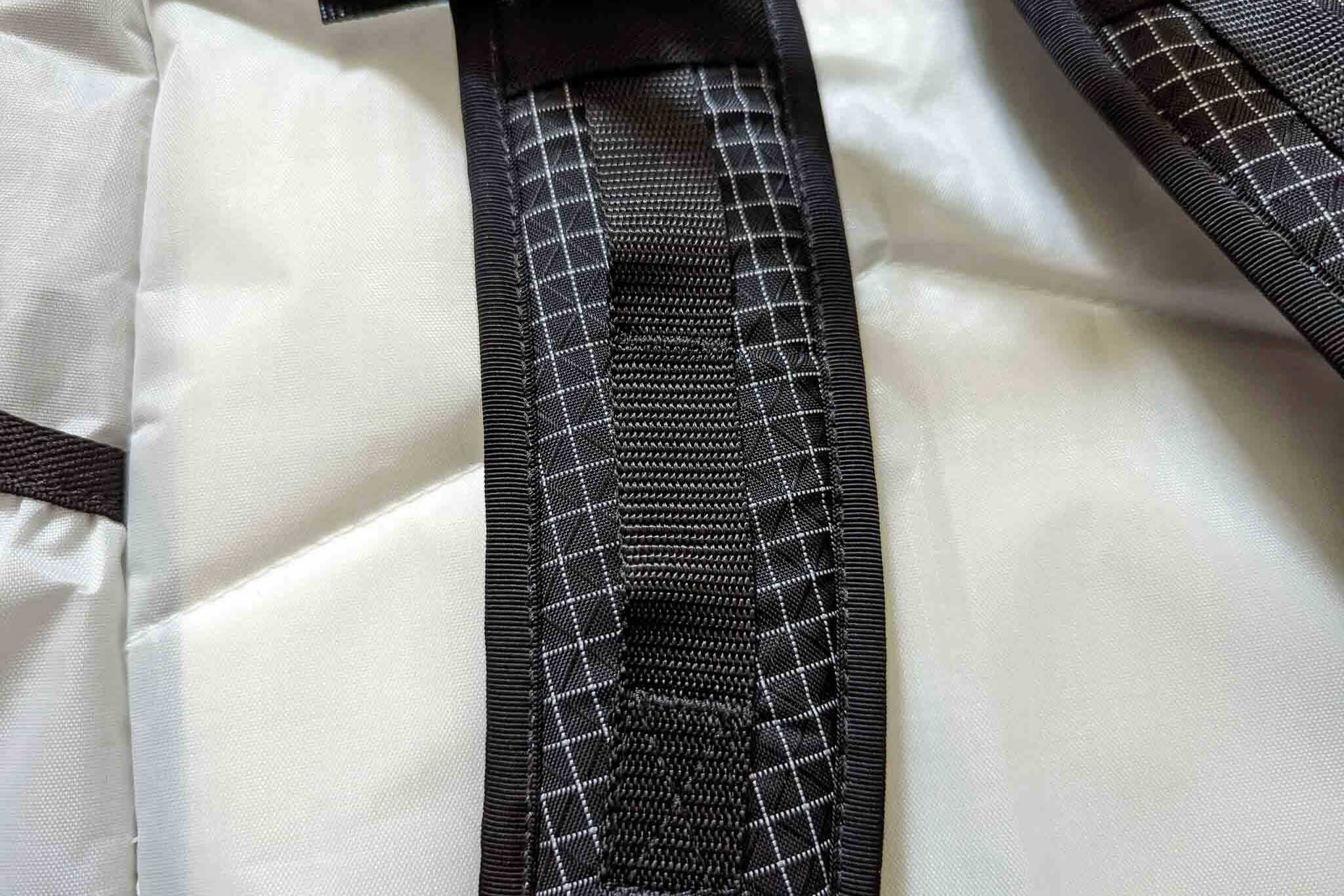 Close-up of a backpack strap with black webbing and white stitching detail, reminiscent of the durable construction found in the Rogue Panda Blue Ridge Handlebar Harness, on a light gray fabric background.