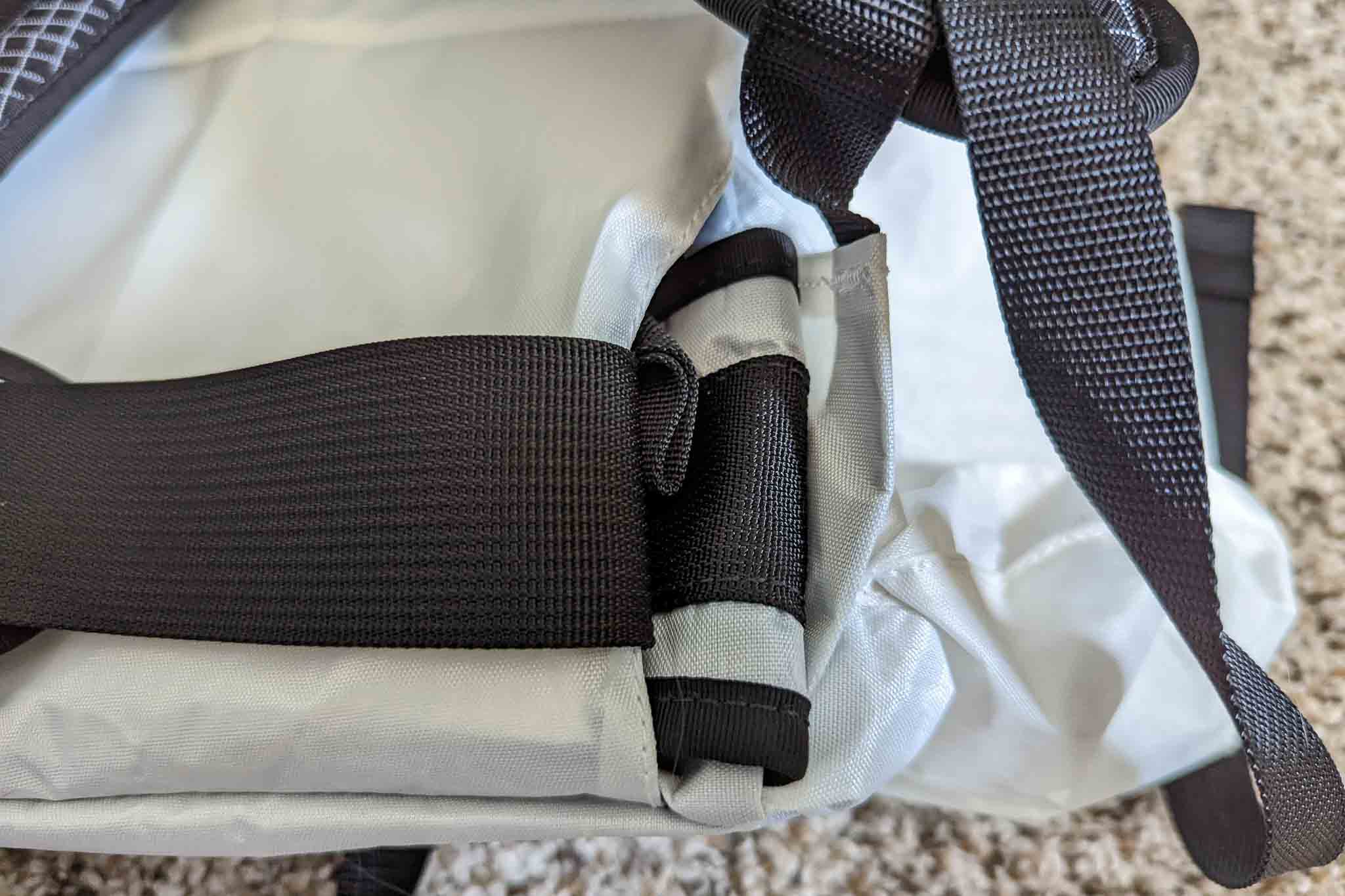 A close-up of a gray backpack shows black straps and buckles on a light carpeted floor, highlighting the Rogue Panda Blue Ridge Handlebar Harness attachment points and its sturdy construction.
