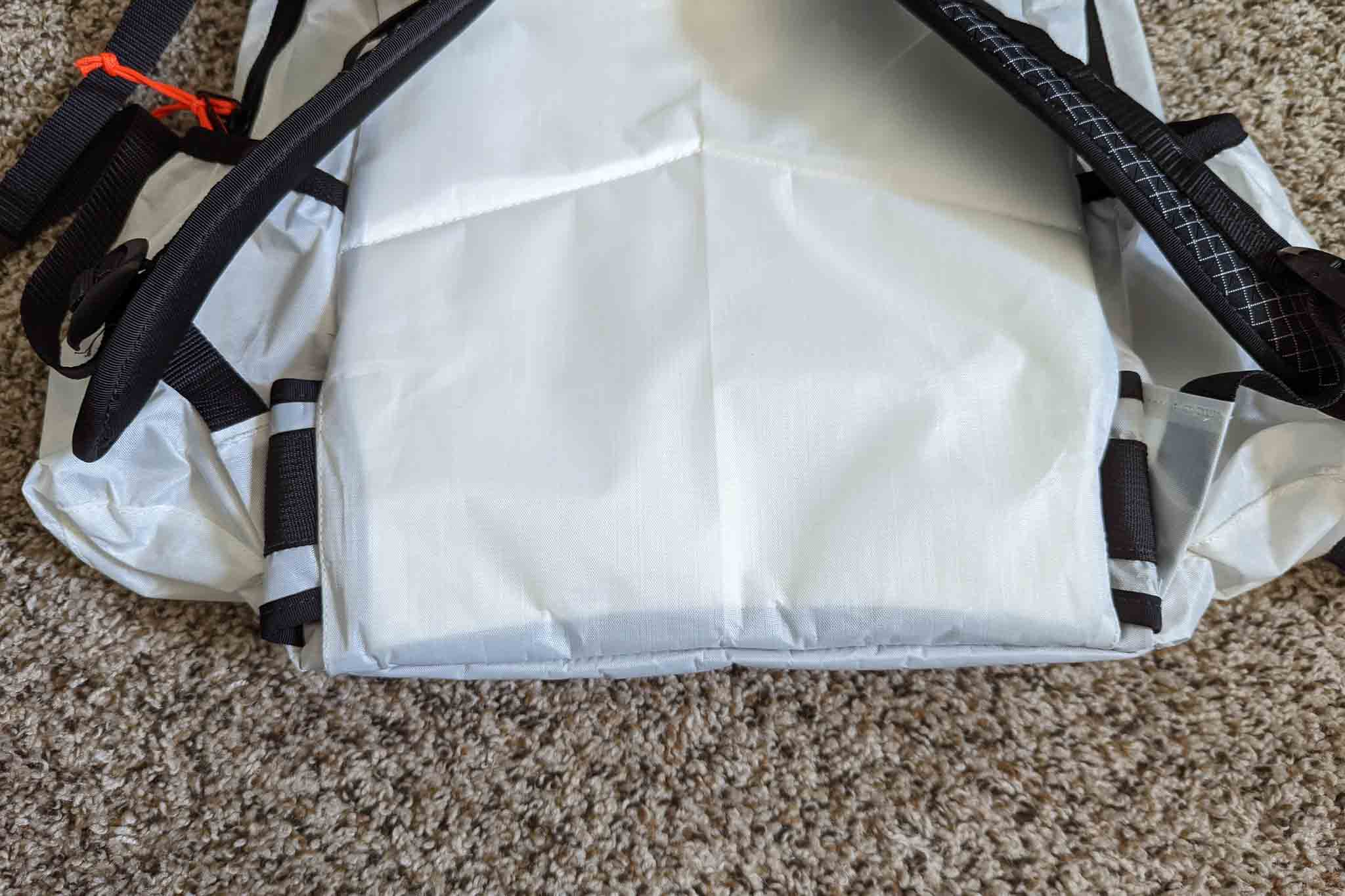 A close-up of the bottom of a light gray backpack with black straps, resting on a beige carpet. The durable fabric and visible stitching evoke the rugged quality of the Rogue Panda Blue Ridge Handlebar Harness.