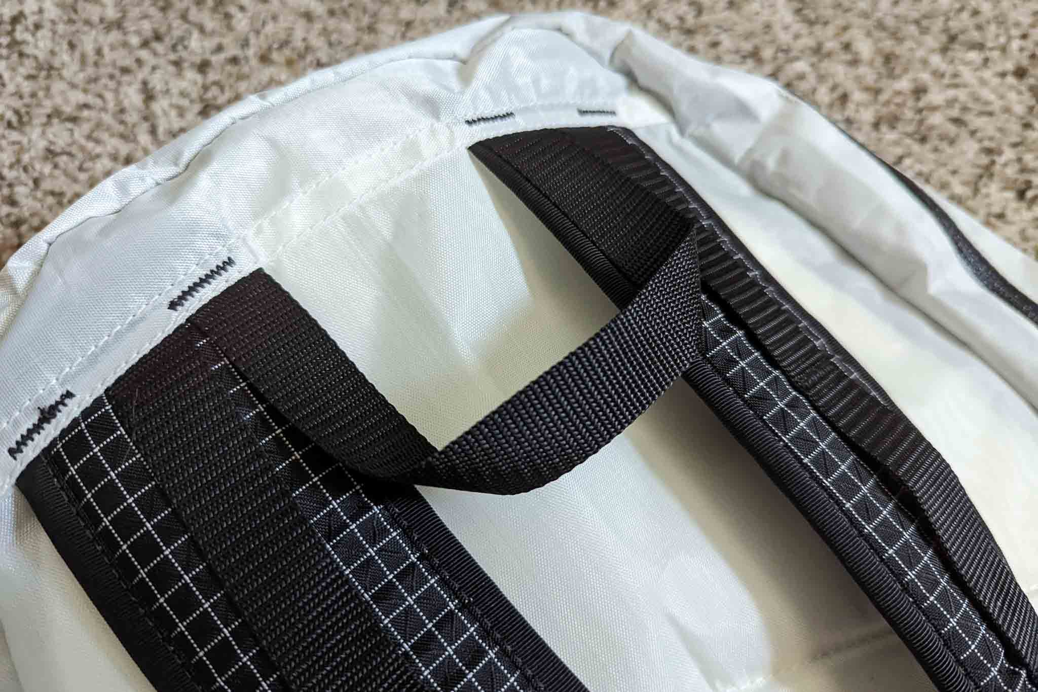 Close-up of a white backpack lying on a carpeted floor, featuring black shoulder straps and a carrying handle with visible stitching—similar in design to the Rogue Panda Blue Ridge Handlebar Harness.