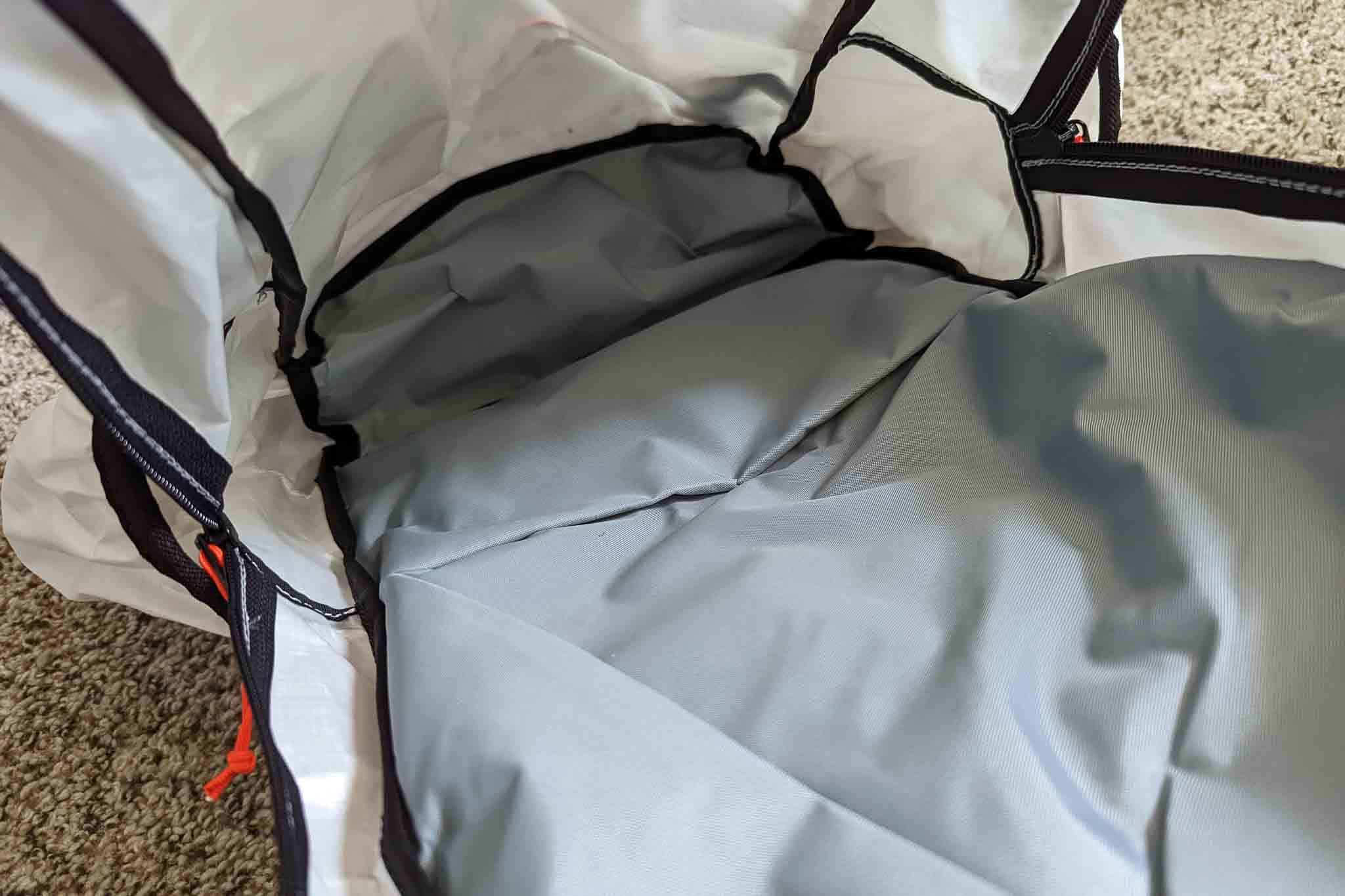 The image shows the inside of an empty gray and white backpack lying open on a carpeted floor, revealing its spacious interior and fabric lining—perfect for carrying gear like the Rogue Panda Blue Ridge Handlebar Harness.