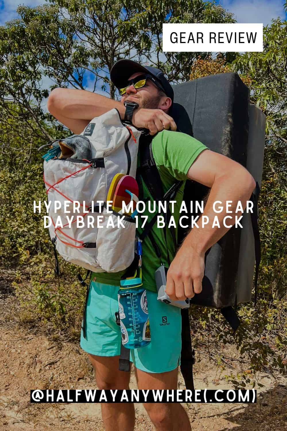A man wearing sunglasses and a green shirt hikes outdoors with a large white Hyperlite Mountain Gear Daybreak backpack and a crash pad on his back. Text overlay reads, GEAR REVIEW: HYPERLITE MOUNTAIN GEAR DAYBREAK 17 BACKPACK.