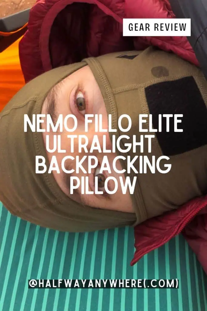 A person in outdoor gear, lying on a green sleeping pad with a balaclava and jacket, tests the NEMO Fillo Elite Ultralight Backpacking Pillow. Text on image: Nemo Fillo Elite Ultralight Backpacking Pillow Gear Review @halfwayanywhere(.com).